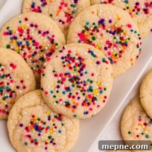 3 Ingredient Sugar Cookies Recipe 12 Sugar cookies topped with sprinkles stacked on a rectangle white plate .