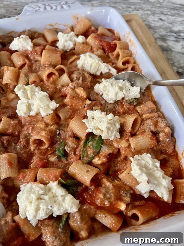 Adding cheese mixture to the top of the baked rigatoni and sausage mixture in baking dish.
