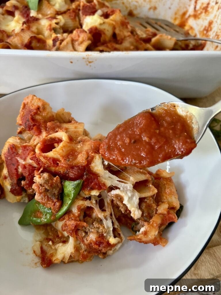 Adding a spoonful of tomato sauce to a portion of baked rigatoni and sausage in pasta bowl.