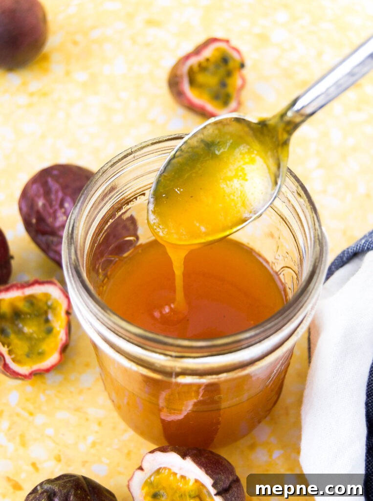 Homemade Passion Fruit Sauce Recipe for Desserts 2 Passion fruit sauce drizzles from a spoon into a mason jar on a yellow surface