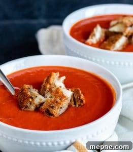 Roasted Red Pepper Tomato Soup Roasted red pepper tomato soup in a white bowl with silver spoon in it. Plus grilled cheese bites on top.