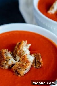 Roasted Red Pepper Tomato Soup Close up shot of soup with grilled cheese bites on top.