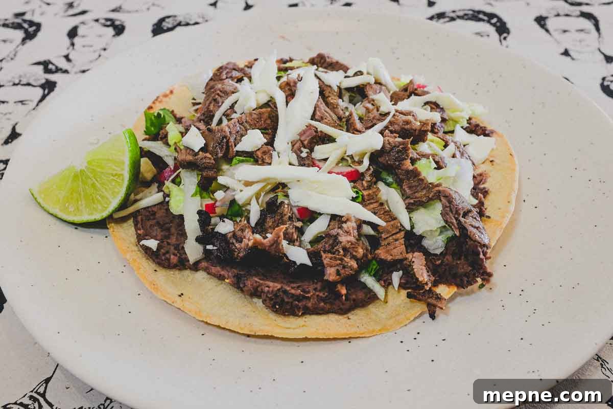 Crisp corn tortillas topped with refried beans, carne asada, salad vegetables and Oaxacan cheese