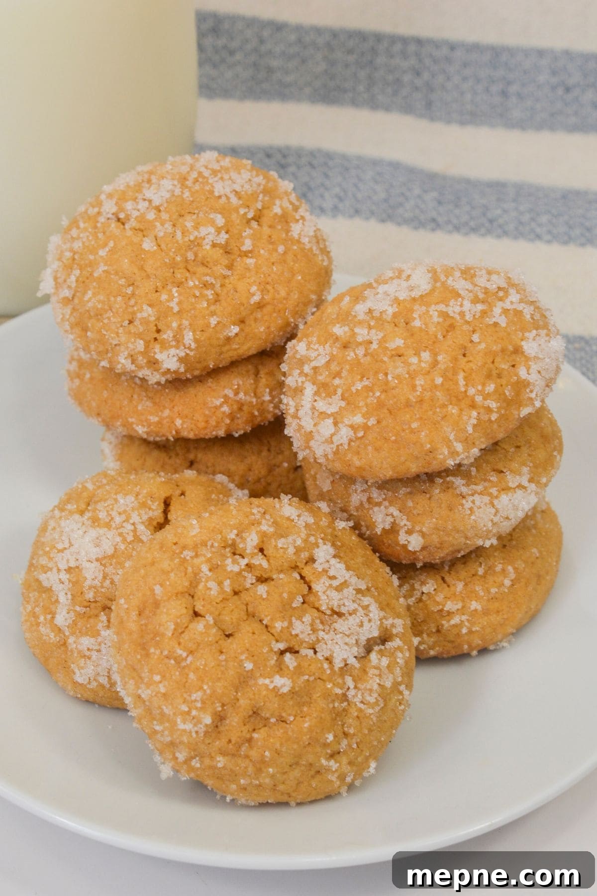Homemade Soft Chewy Ginger Molasses Cookies Recipe 2 A white plate with stacks of round, golden Ginger Molasses Cookies coated in granulated sugar, set in front of a blue and white striped cloth.