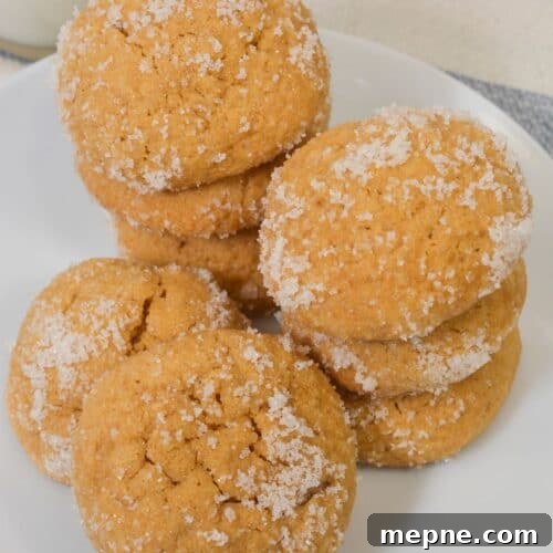 Homemade Soft Chewy Ginger Molasses Cookies Recipe 11 A white plate with stacks of round, sugar-coated Ginger Molasses Cookies on a table, with part of a glass of milk visible in the background.