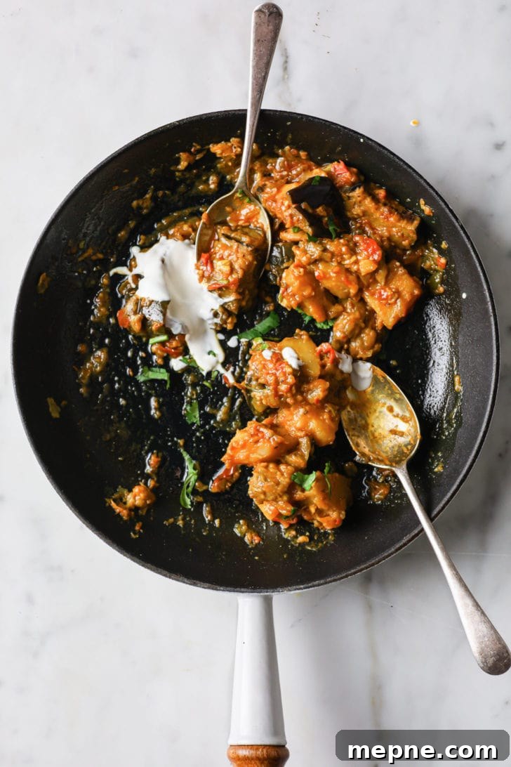 Aloo Baingan: Indian Eggplant and Potato Curry 13 Half-eaten Aloo Baingan in a skillet with two silver spoons