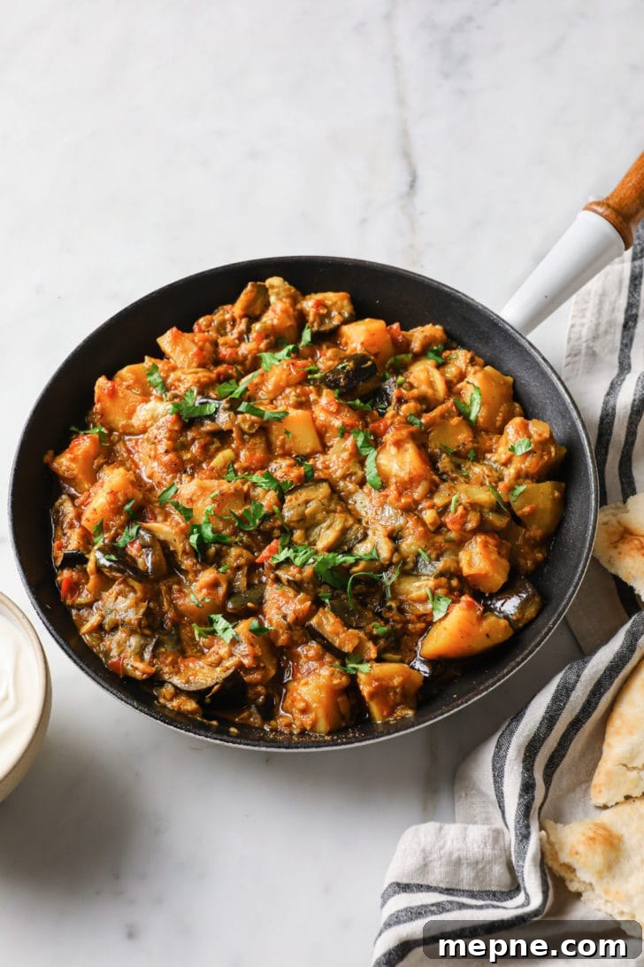 Aloo Baingan: Indian Eggplant and Potato Curry 4 Aloo Baingan in a black skillet with a white and wooden handle
