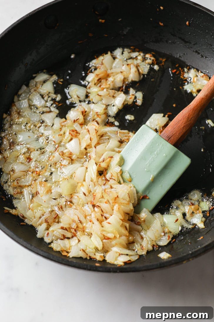 Aloo Baingan: Indian Eggplant and Potato Curry 7 Chopped yellow onions being sautéd in a skillet.