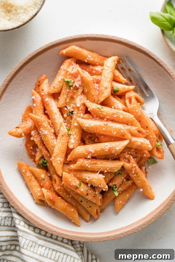 Bowl of creamy tomato pasta sprinkled with fresh grated Parmesan.