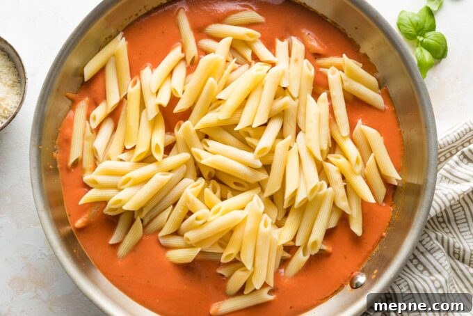 Al dente penne added to tomato cream sauce in a skillet.