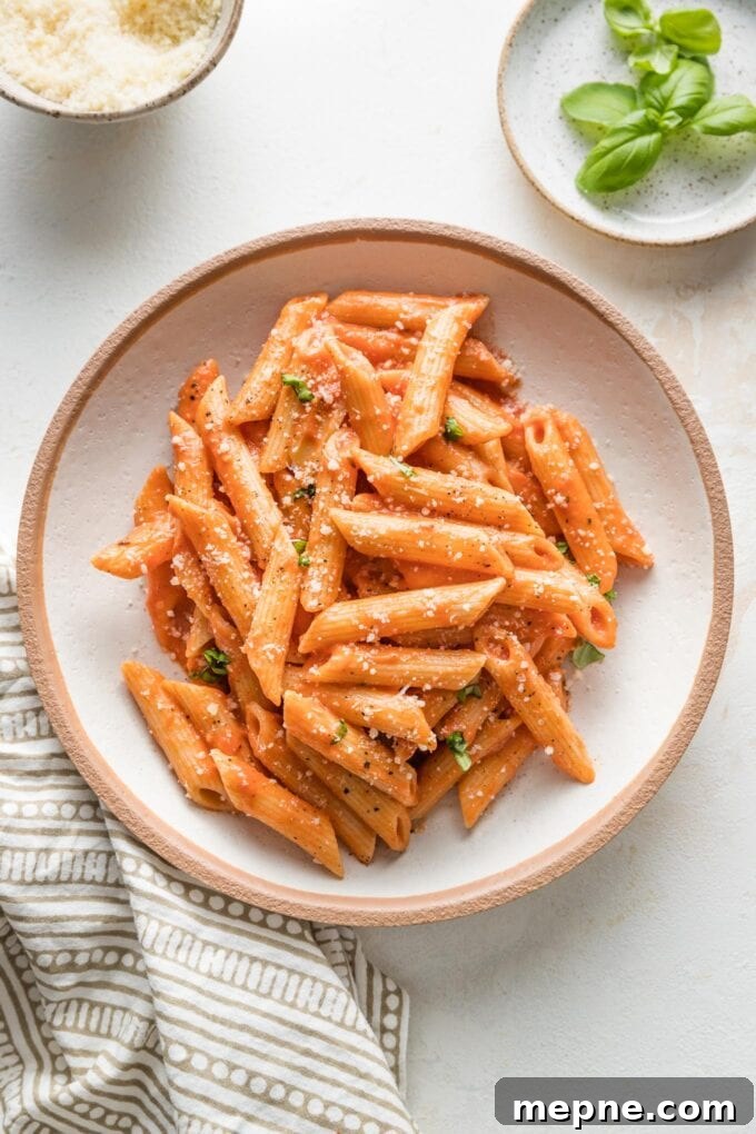 Bowl of creamy tomato pasta sprinkled with fresh grated Parmesan.
