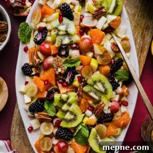 A festive and colorful thanksgiving fall fruit salad on a large white platter garnished with mint.