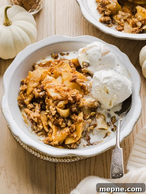Apple pumpkin crisp with vanilla ice cream in a white bowl.