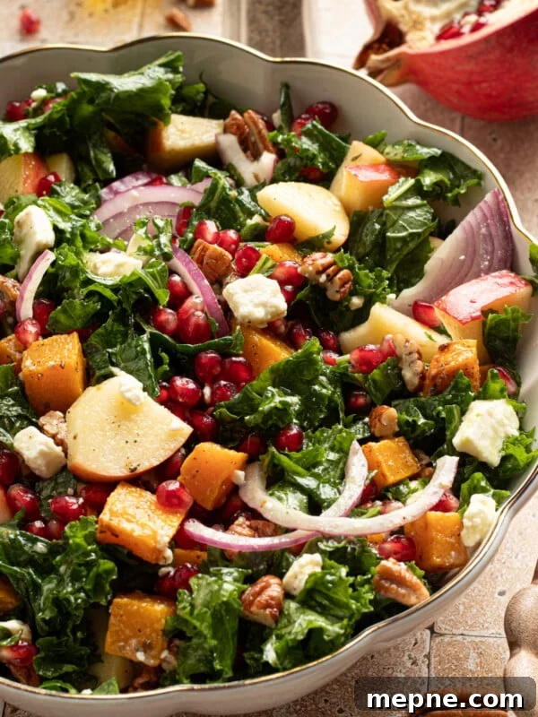Kale and butternut squash salad with apple and pomegranate seeds in a large bowl.