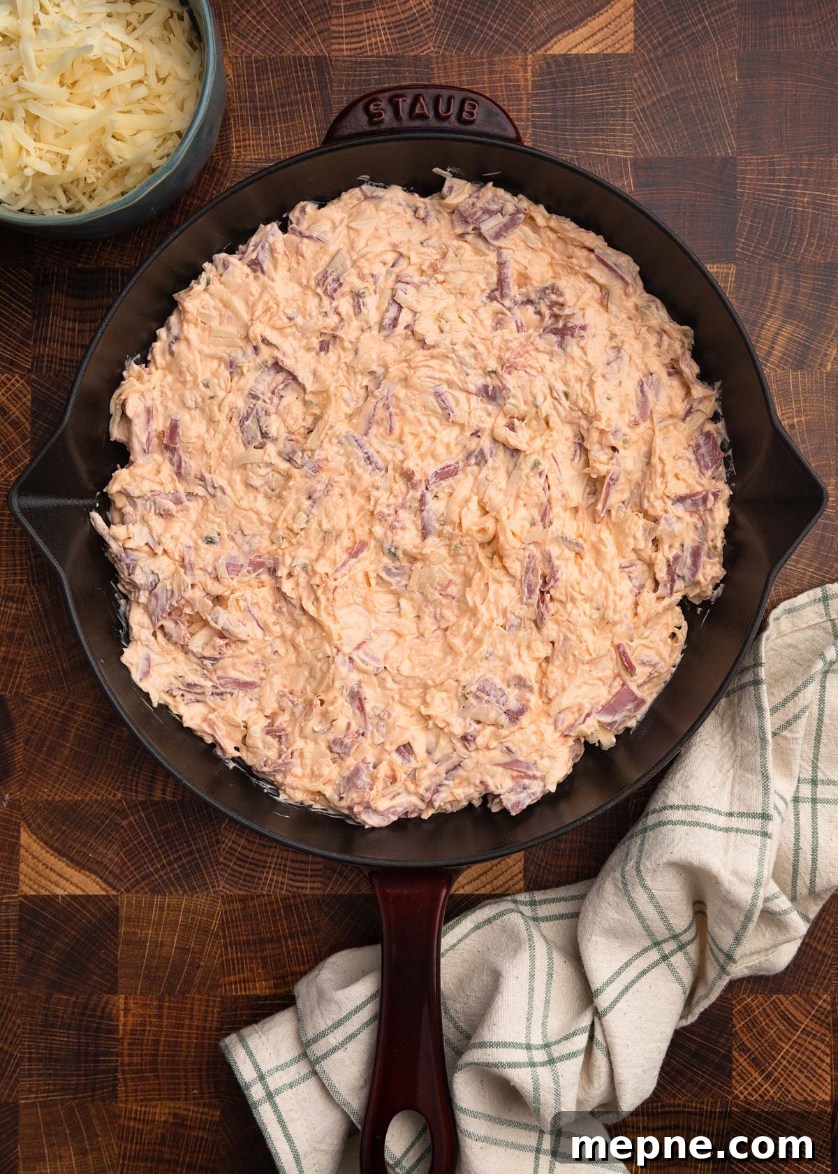 overhead photo of unbaked reuben dip in a staub cast iron skillet on a butcher block board