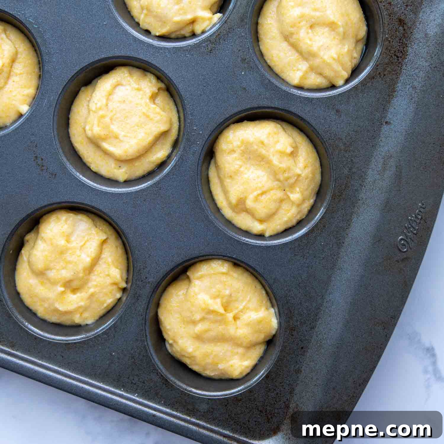 Moist Gluten Free Corn Muffins Recipe 6 unbaked gluten-free cornbread muffins in a muffin pan.