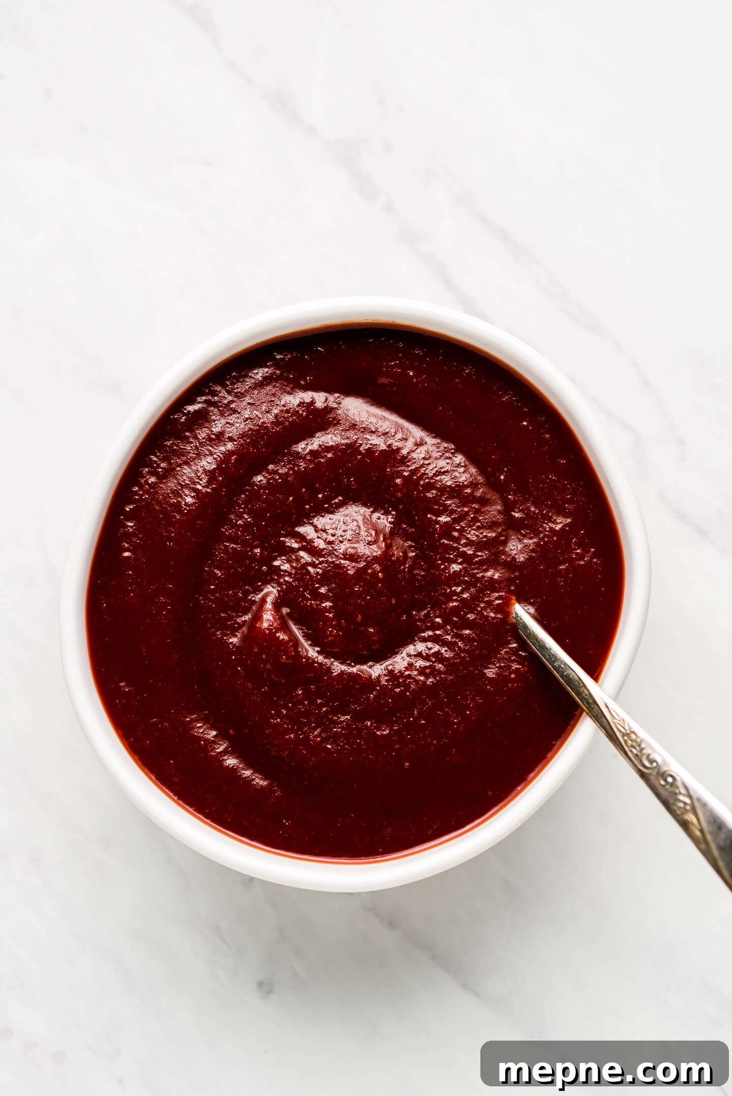 A bowl of bbq sauce with a spoon in the side.
