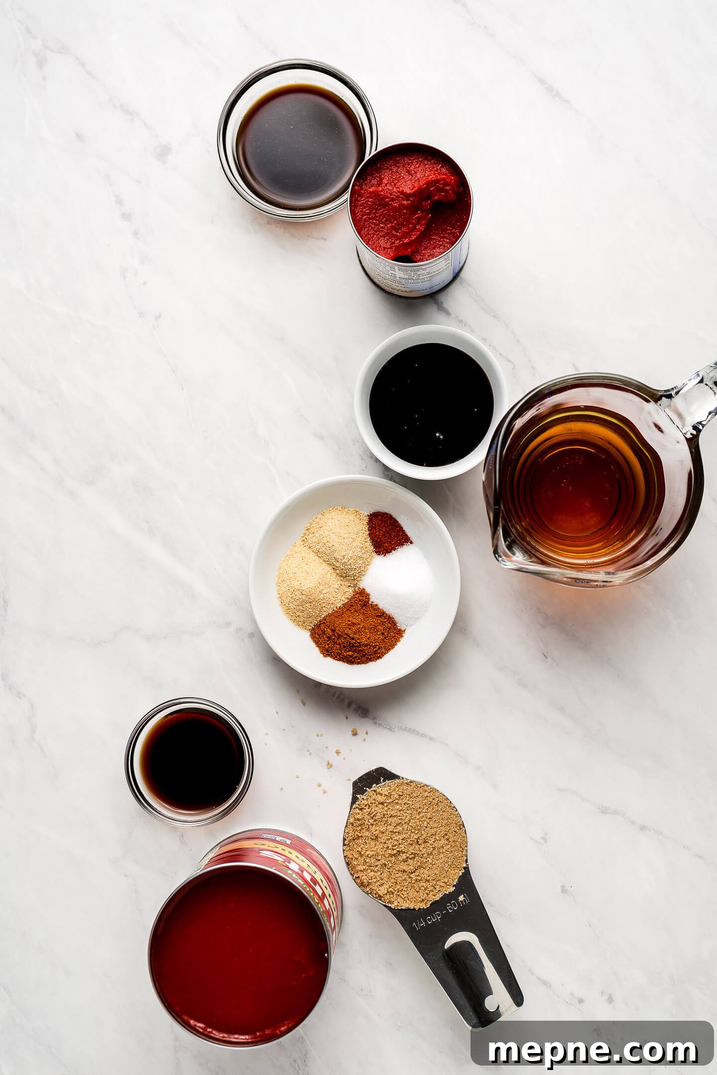 Ingredients on a marble surface- tomato paste, sauce, spices, sugar, soy sauce, and vinegar.