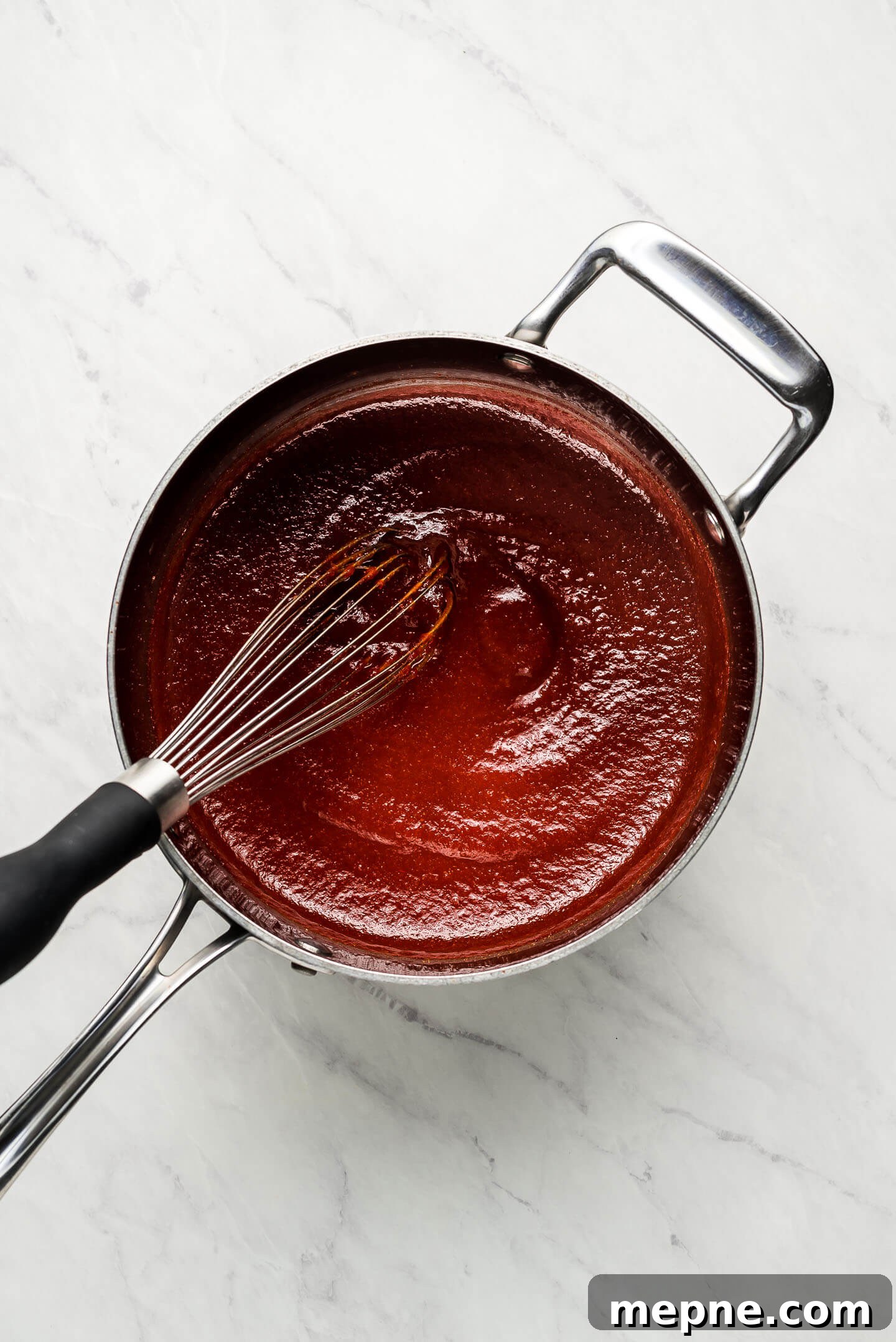 A pot of homemade barbecue sauce with a whisk.