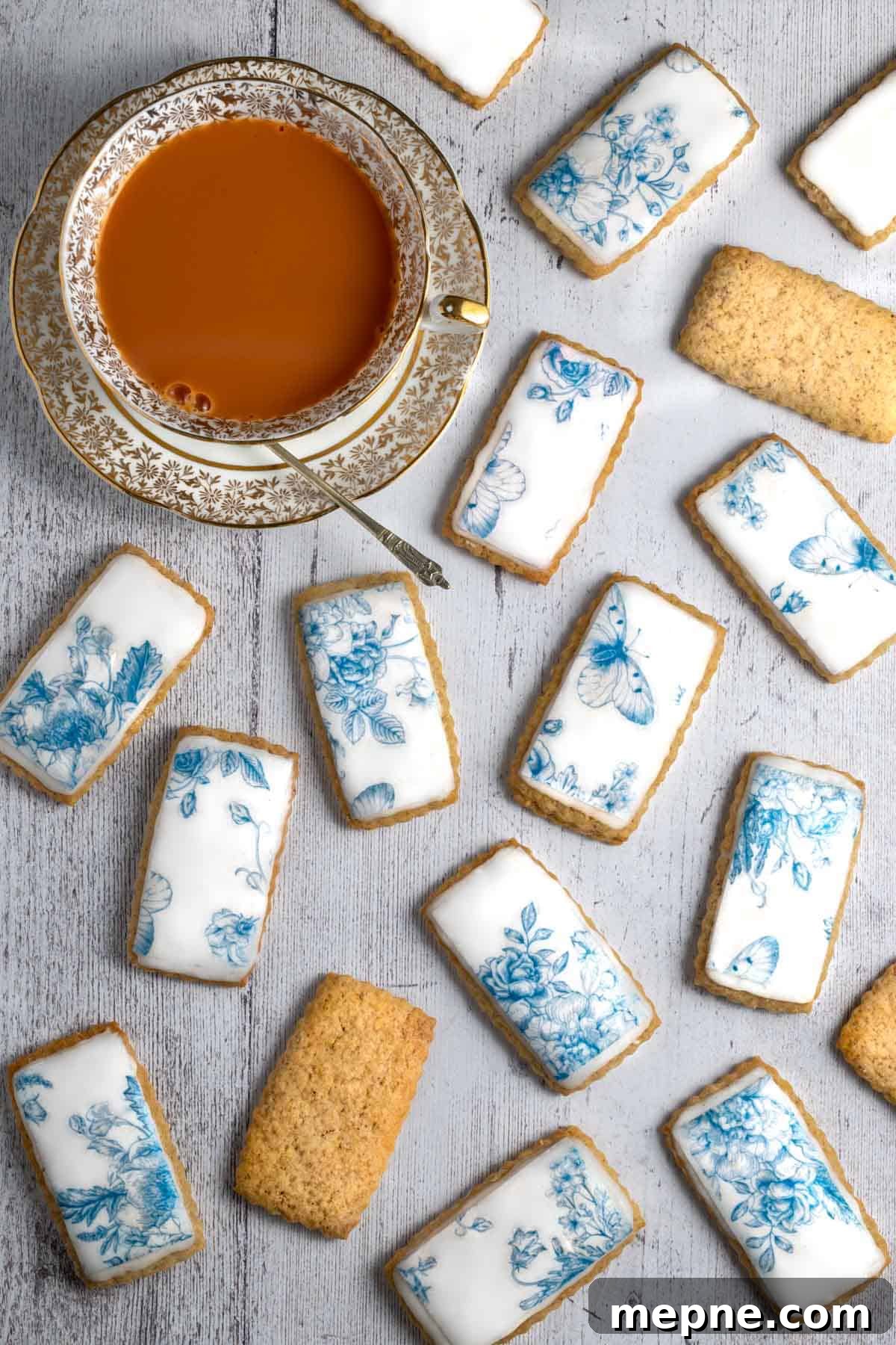 Old Fashioned South African Spice Biscuits (Soetkoekies) Recipe 6 Spice biscuits, or soetkoekies, scattered across a white table with a cup of tea on the side.