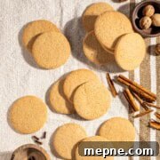 Old Fashioned South African Spice Biscuits (Soetkoekies) Recipe 7 Outydse soetkoekies scattered across a textured tea towel, surrounded by nutmeg, cloves and cinnamon sticks.