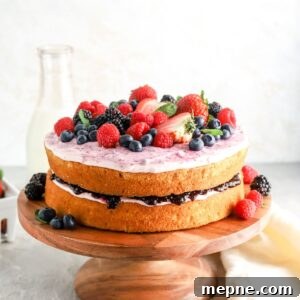 Mixed Berry Layer Cake with Fresh Berries 12 A two layer cake on a cake stand with jam and frosting in the middle and berries on top.