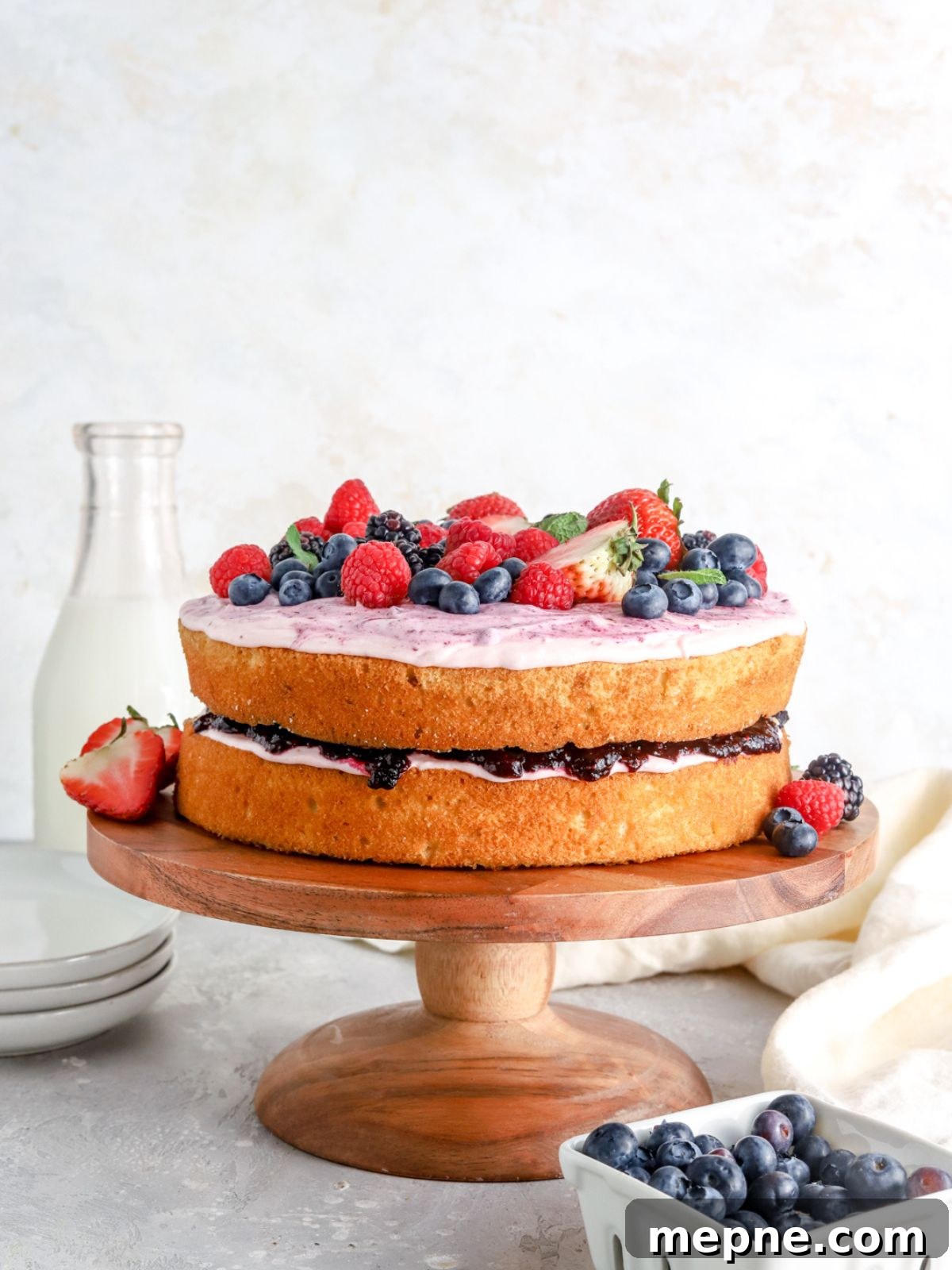 Mixed Berry Layer Cake with Fresh Berries 7 A two layer cake with jam and frosting and berries on a cake stand.