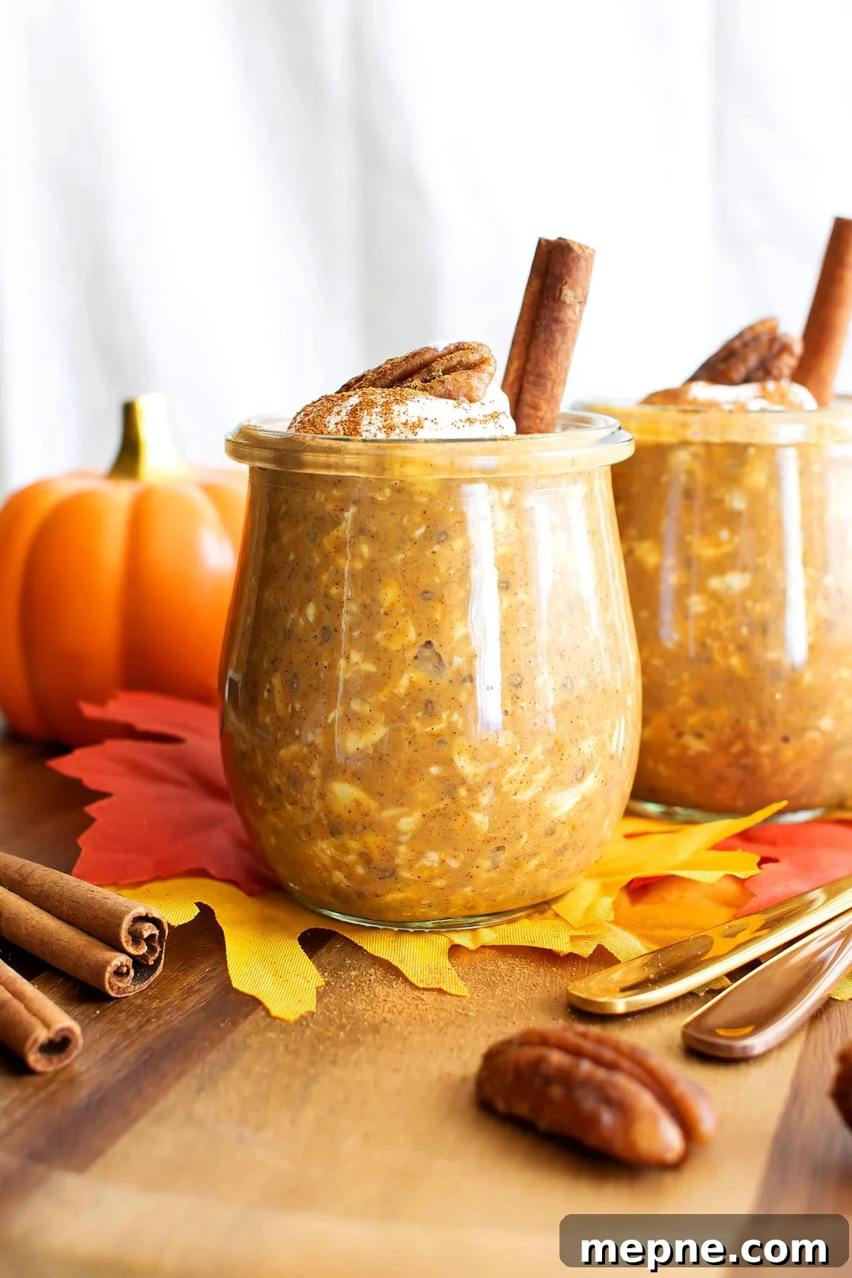 Two jars of pumpkin overnight oats are served on a fall breakfast table with pumpkins and leaves.