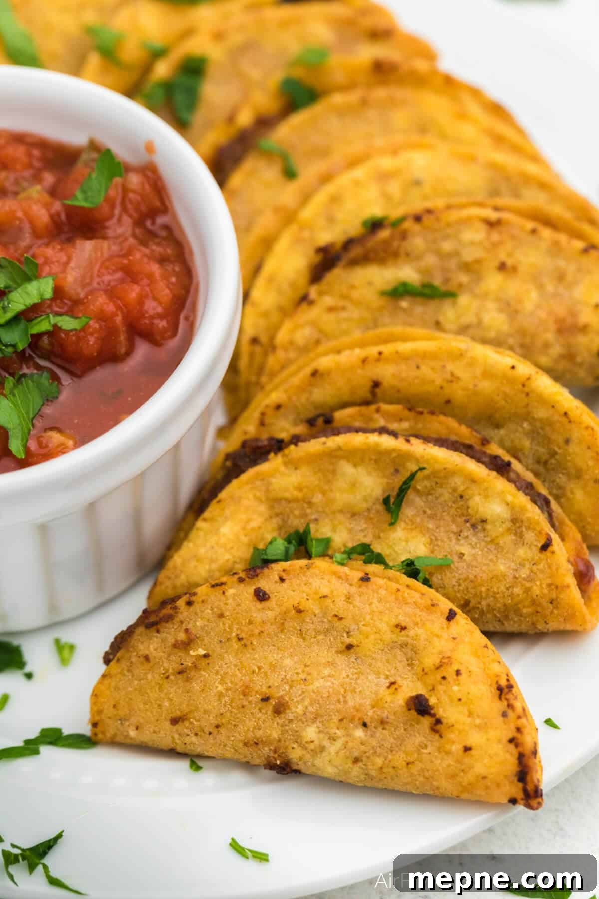 Air Fryer Frozen Mini Tacos: Crispy in Minutes 2 Air fried mini tacos on a plate with a bowl of salsa. Ready to serve.