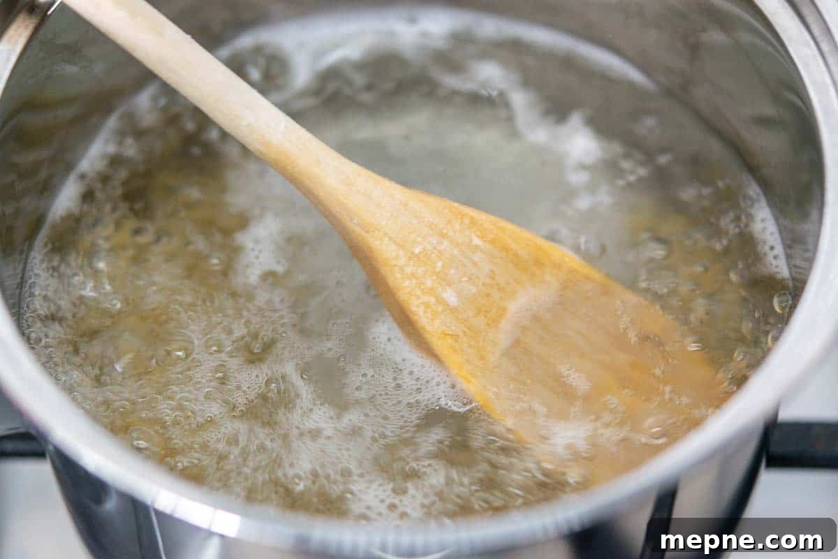 Ham and Egg Salad Recipe with Creamy Dijon Dressing 3 pasta cooking in a pan of boiling water with a wooden spoon resting on the surface of the water.
