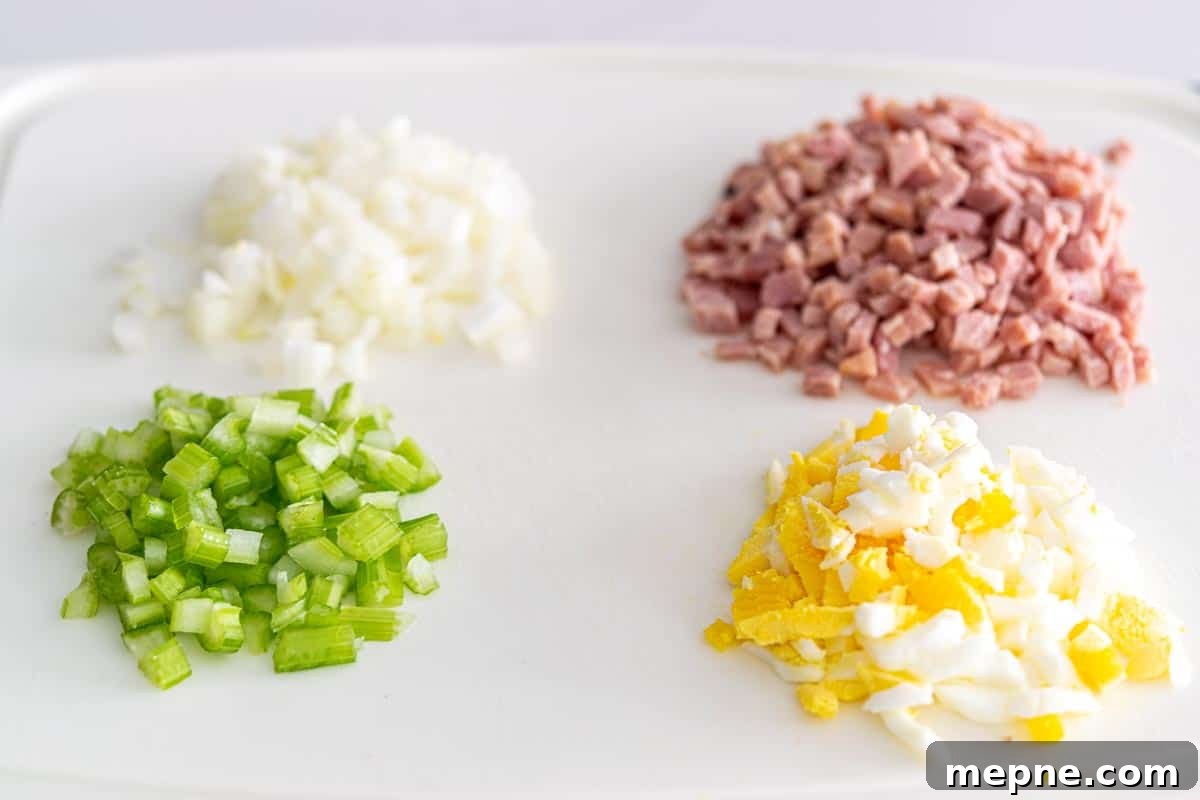 Ham and Egg Salad Recipe with Creamy Dijon Dressing 4 a cutting board with piles of diced onions, ham, celery, and hard-boiled egg.