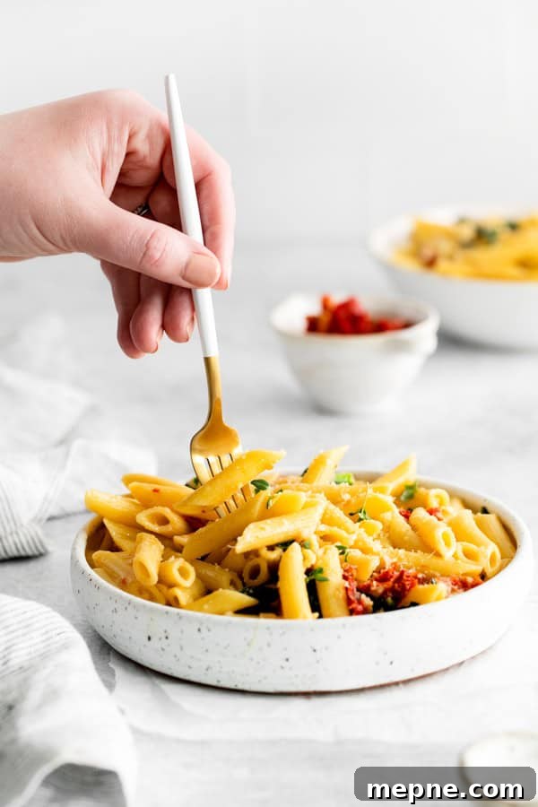 Sun-Dried Tomato and Kale Pasta Recipe 6 A hand holding a fork picking up a bite of Sun dried Tomato and Kale Pasta.