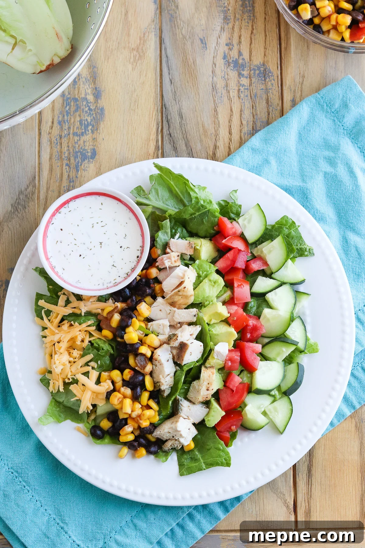 Grilled Chicken Fajita Salad Recipe with Avocado & Lime 2 A white dinner plate full of bed of lettuce, topped with black bean and corn salsa, grilled fajita chicken, cucumber, tomatoes, cheese and served with ranch.