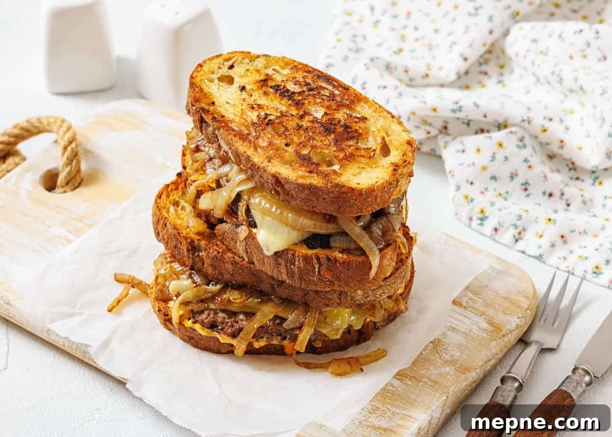31 Southern Recipes That Belong in Your Dinner Rotation 11 A stack of two patty melt sandwiches with caramelized onions and melted cheese on toasted bread, placed on parchment paper atop a wooden board.