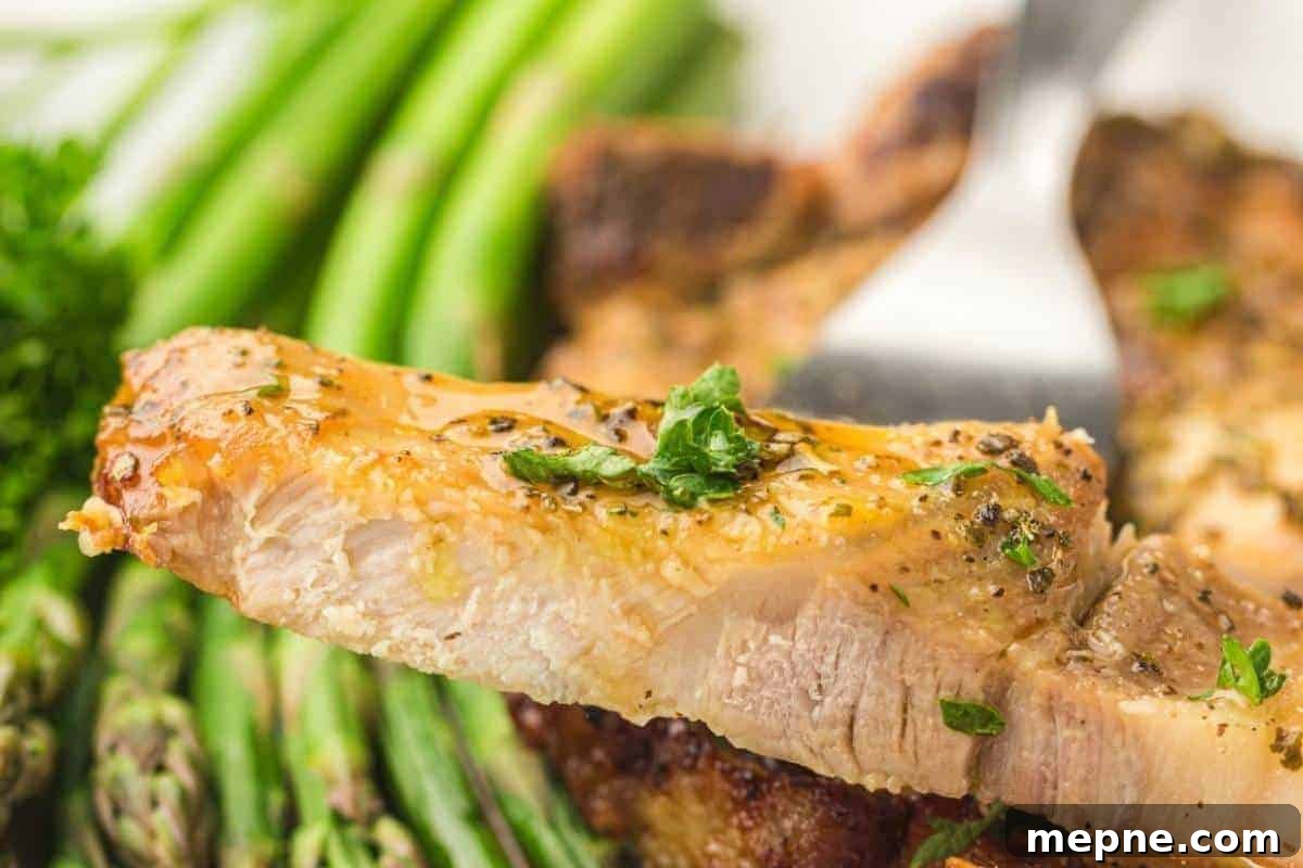 31 Southern Recipes That Belong in Your Dinner Rotation 13 A close-up of a seasoned pork chop slice garnished with herbs, held by a fork, with asparagus spears in the background.