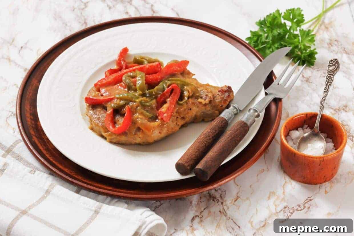 31 Southern Recipes That Belong in Your Dinner Rotation 15 Smothered Pork Chops on a white plate, served with a fork and knife, next to a small bowl of salt and a sprig of parsley.