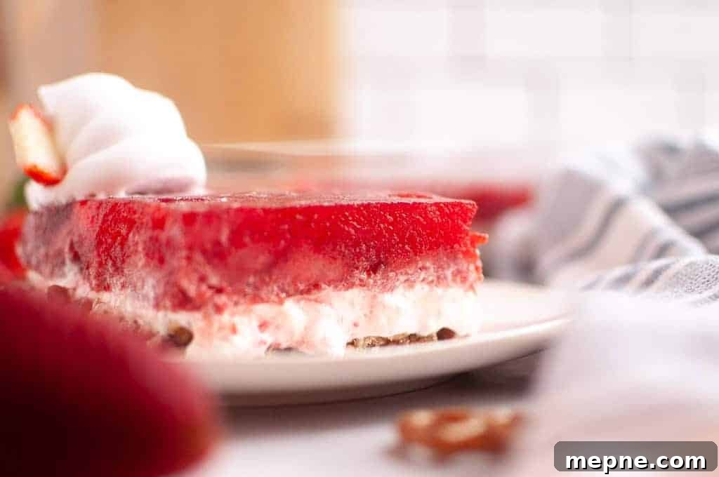 31 Southern Recipes That Belong in Your Dinner Rotation 3 A slice of strawberry pretzel salad with whipped cream on a white plate, showing layers of red gelatin, creamy filling, and pretzel crust.