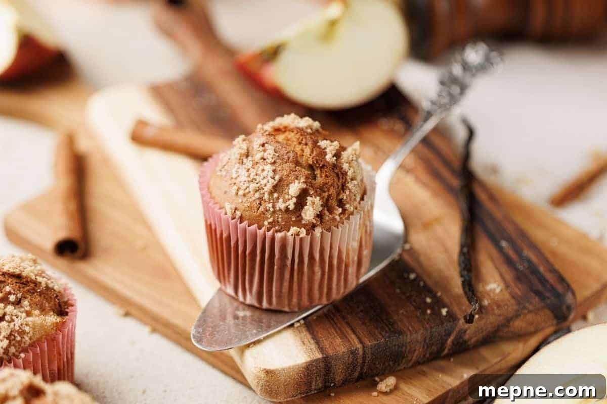 31 Southern Recipes That Belong in Your Dinner Rotation 22 A muffin with crumb topping sits on a metal spatula over a wooden cutting board, surrounded by apple slices, cinnamon sticks, and a vanilla bean.
