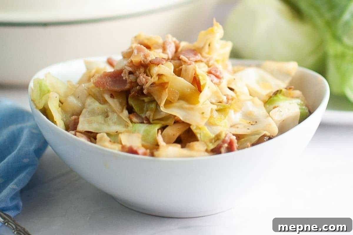 31 Southern Recipes That Belong in Your Dinner Rotation 23 A white bowl filled with fried cabbage with pieces of bacon sits on a white surface with a blue cloth nearby.