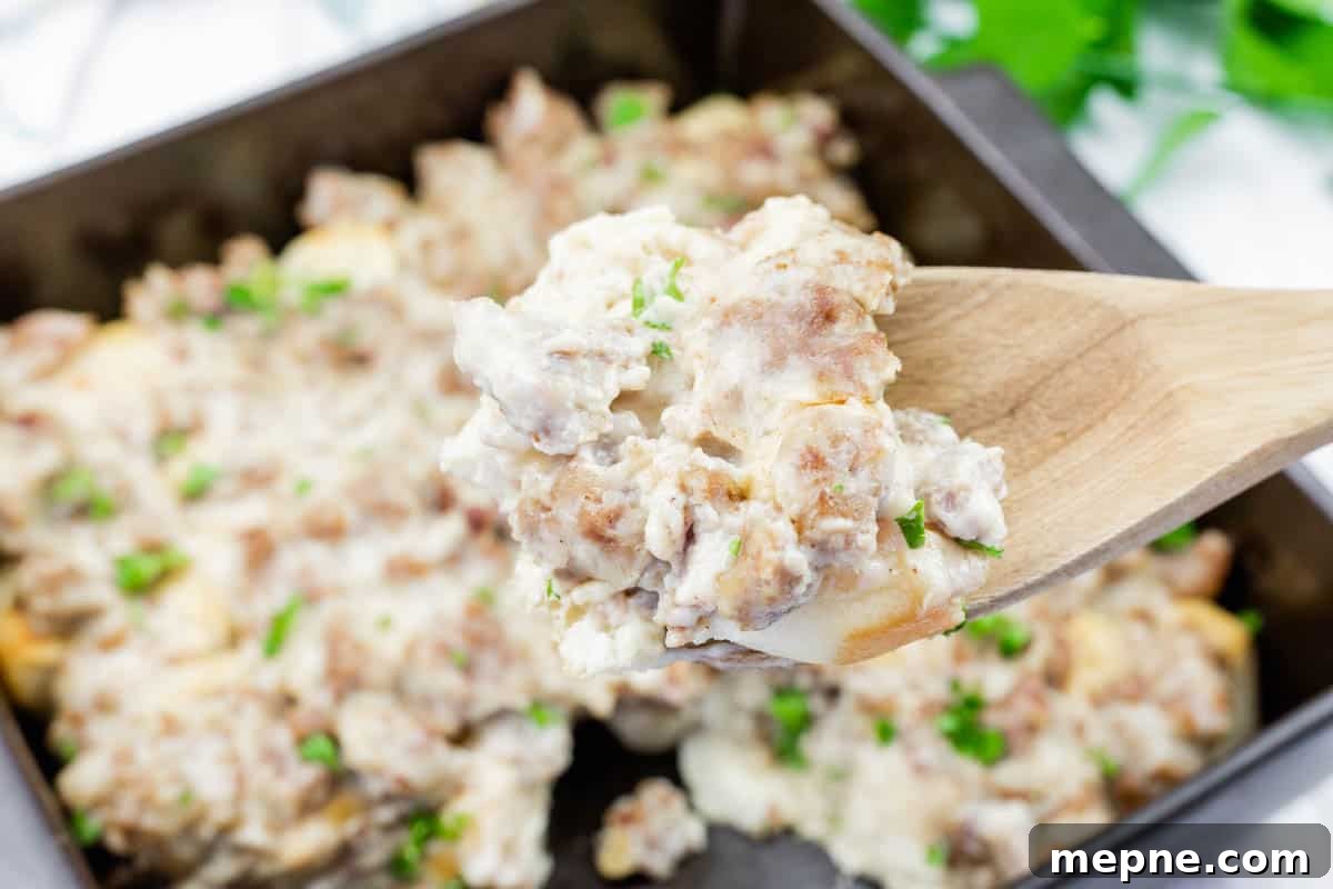 31 Southern Recipes That Belong in Your Dinner Rotation 25 A wooden spoon holds a serving of biscuits and gravy with sausage, over a baking dish filled with the same dish, garnished with chopped herbs.