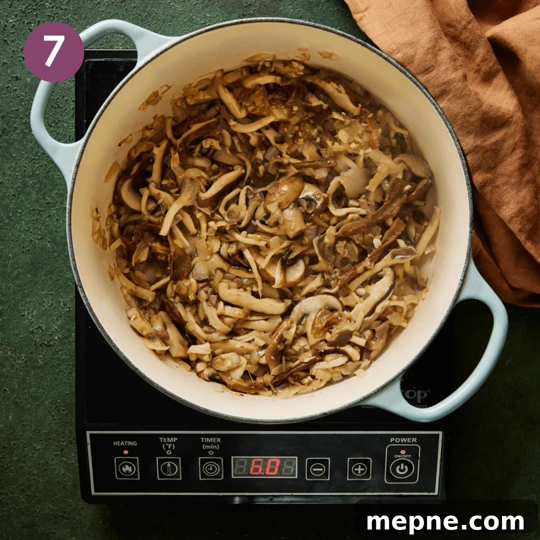 sliced mushrooms sautéing in a light blue dutch oven.