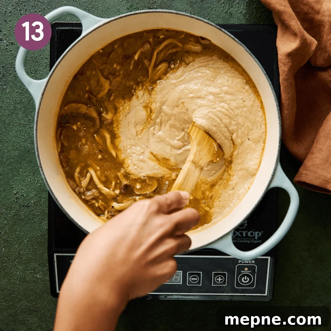 woman's hands stirring creamy mushroom soup into a pot of mushroom soup.