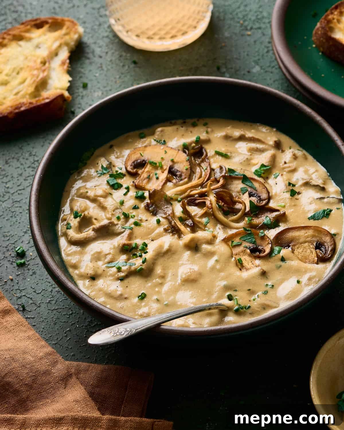 angled backlit shot of creamy vegan mushroom soup in a green bowl with bread and wine in the background.
