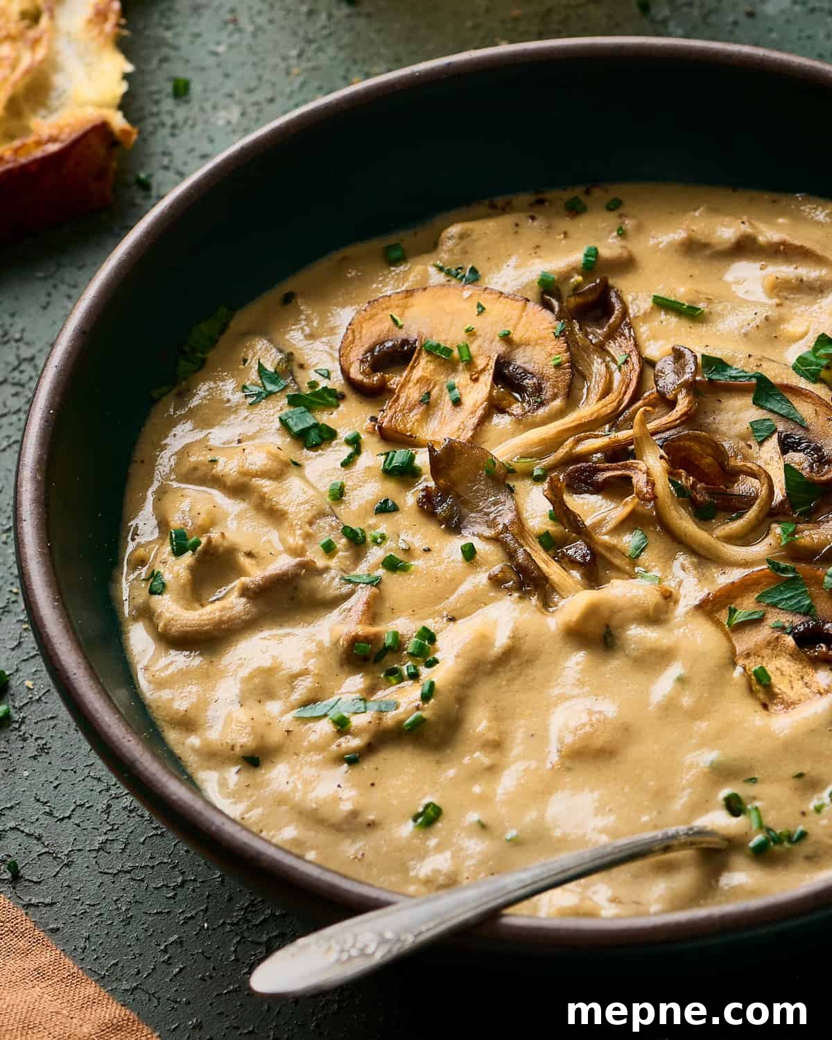 closeup backlit shot of creamy vegan mushroom soup in a green bowl with bread in the background.