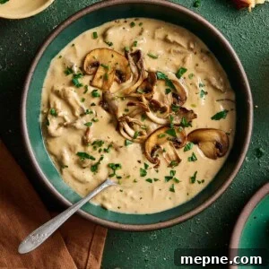 creamy vegan mushroom soup with seared mushrooms on top in a green ceramic bowl on a green table.
