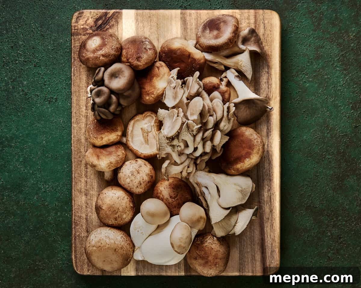 a variety of beautiful whole mushrooms on a wooden cutting board on a green surface.