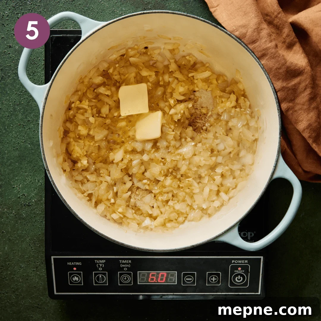 two pats of vegan butter melting in a blue dutch oven with sauteed garlic and onions.