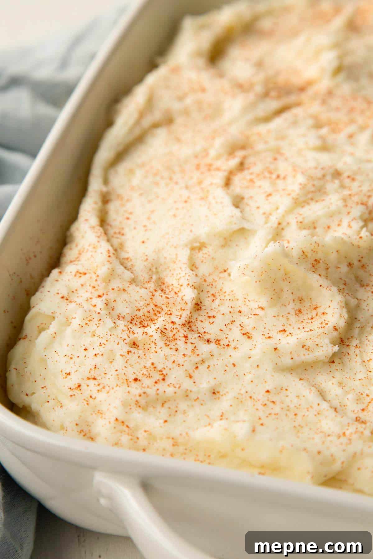 creamy mashed potatoes in a casserole dish, topped with a dusting of paprika.