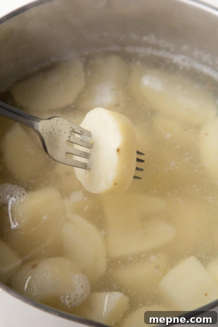 fork piercing a cooked potato above a pot of water and more potatoes.