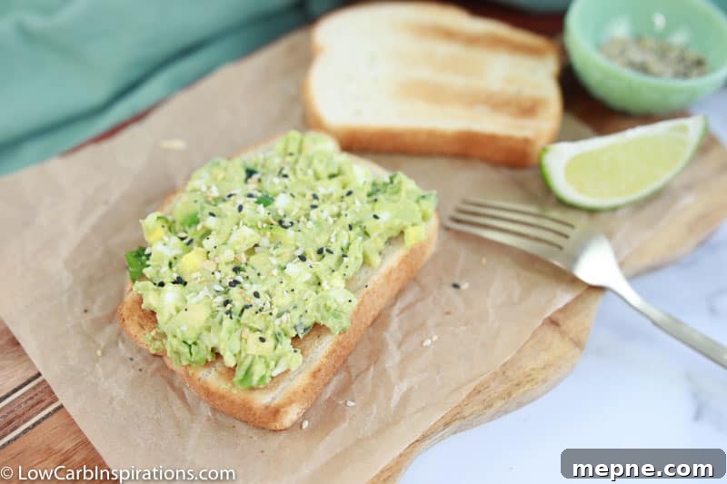 avocado egg salad recipe made on brown parchment paper with a fork, lime and seasonings on the side